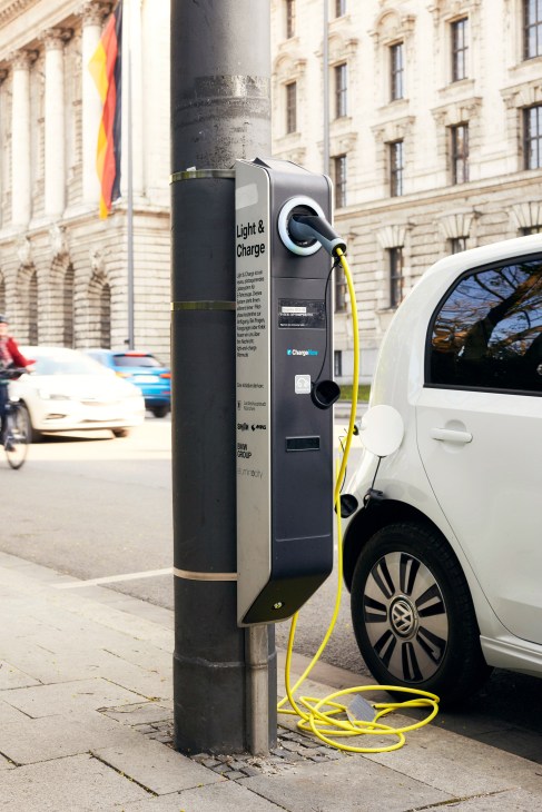 Eluminocity smart lamppost charging station with yellow cable attached to white electric car on Munich street