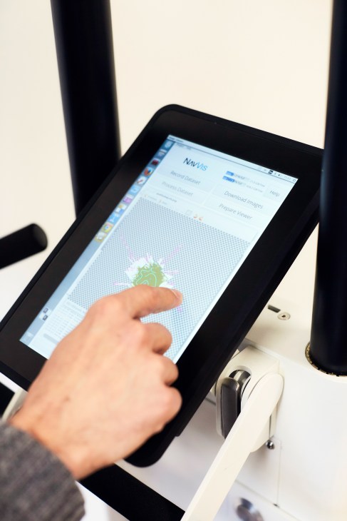 Hand touching a tablet screen displaying NavVis mapping software with green data visualization