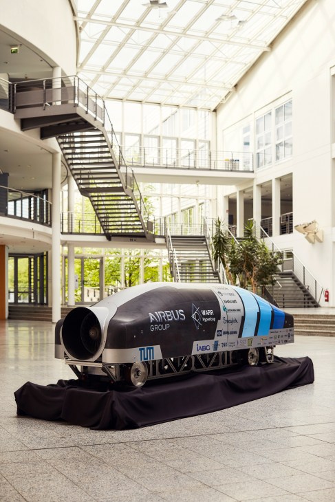 Hyperloop pod prototype displayed in a modern atrium with glass ceiling and metal stairs.