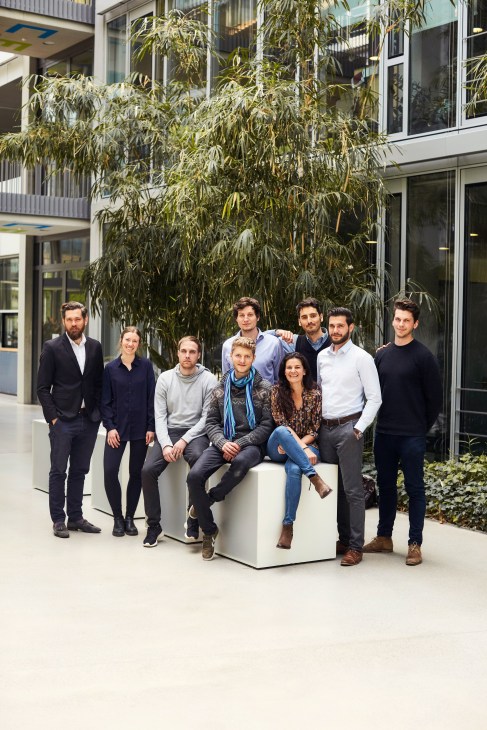 Sono Motors team of nine people posing together in front of a building with climbing ivy.