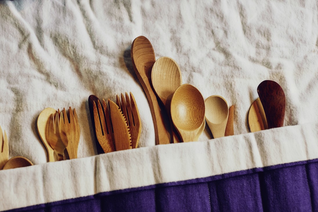 Wooden cutlery including forks, knives and spoons arranged in a cloth holder.