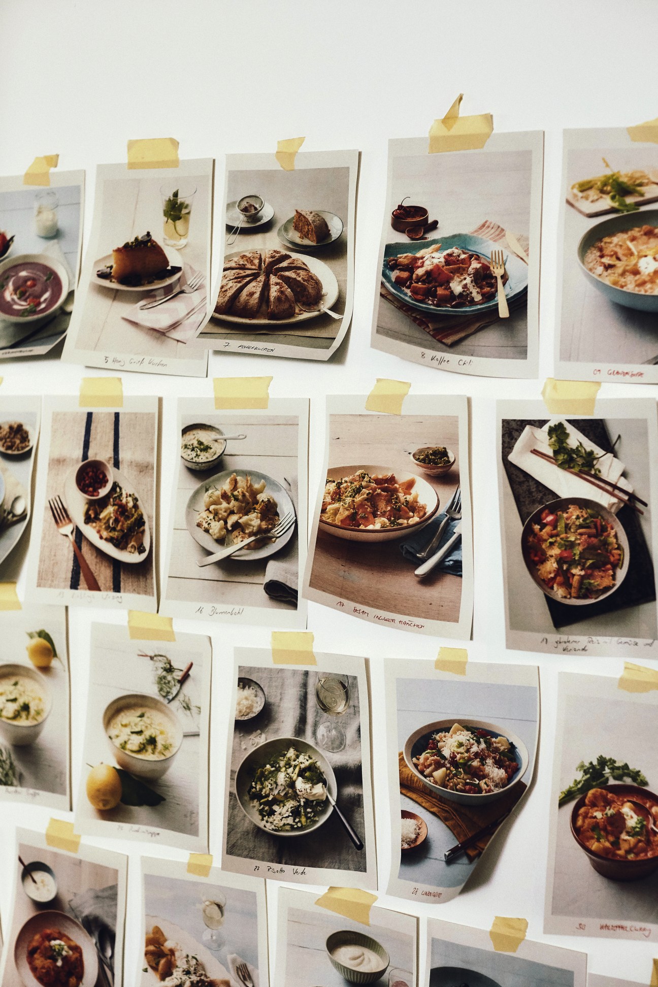 Printed food photographs pinned to a wall with yellow sticky notes, showing various plated dishes and recipes.