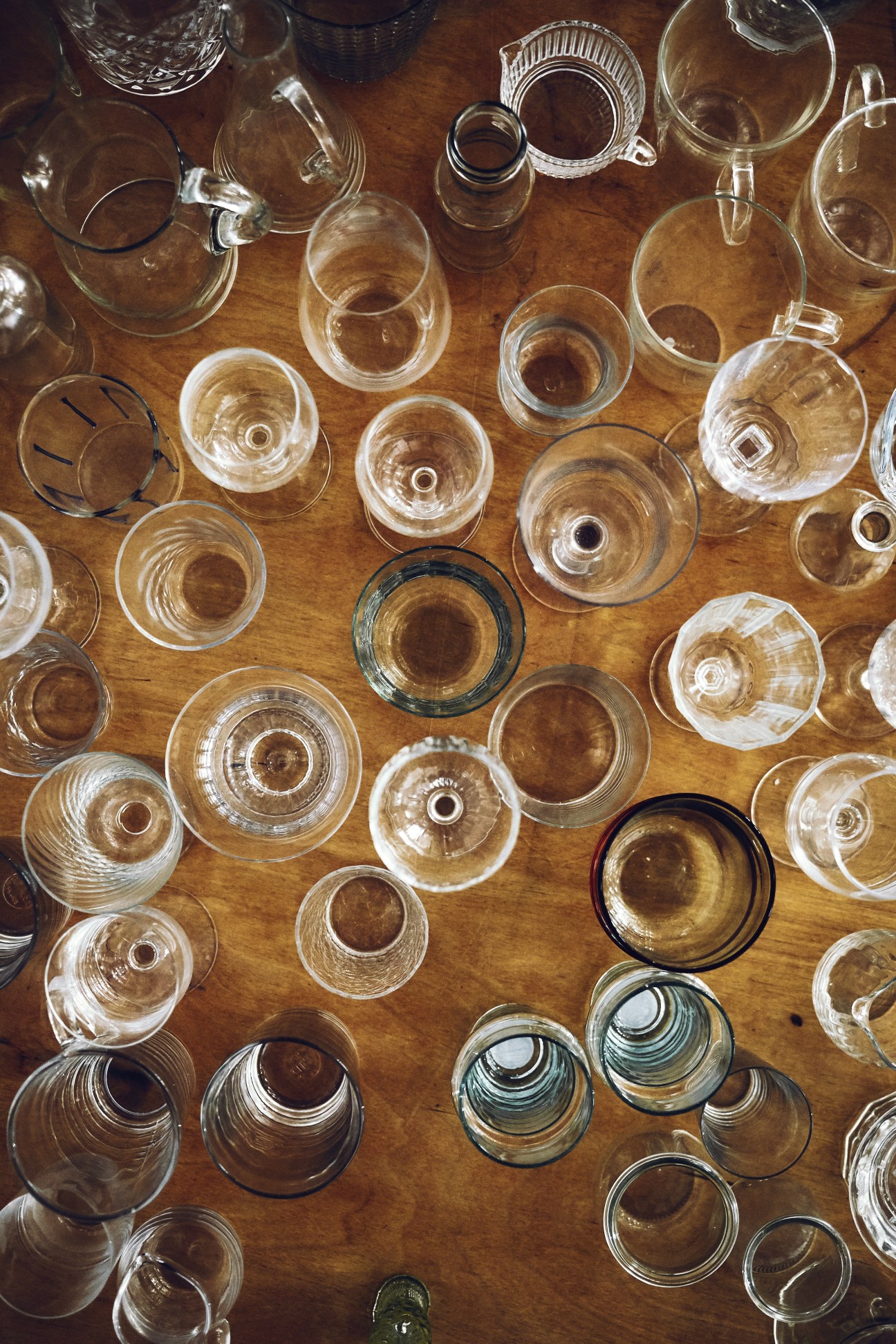 Overhead view of numerous clear and tinted glass cups and mugs arranged on a wooden surface.
