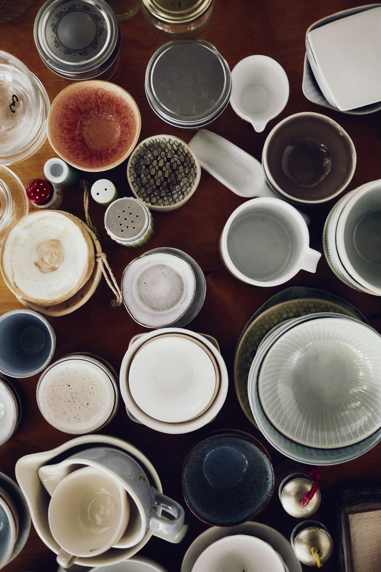 Overhead view of various ceramic bowls, plates, cups and containers arranged on a dark wooden surface.