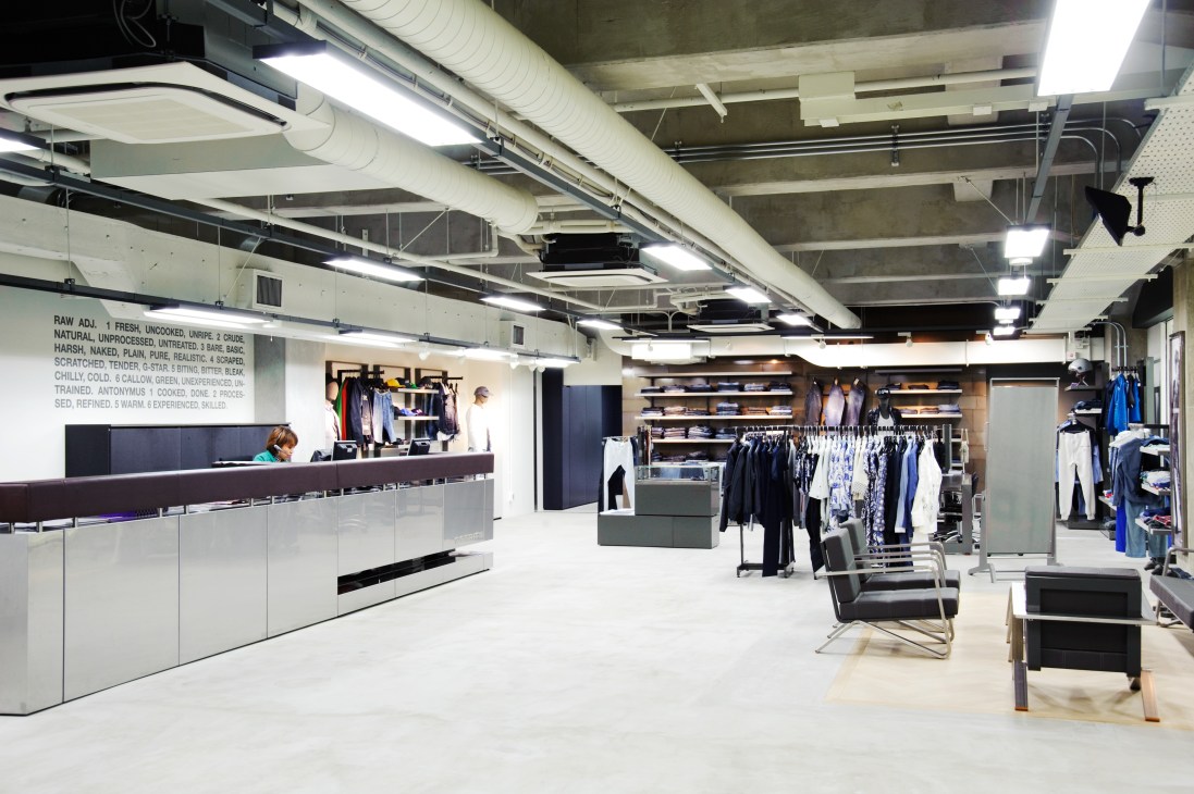 G-Star showroom with modern minimalist design featuring white counter, clothing displays and industrial ceiling.