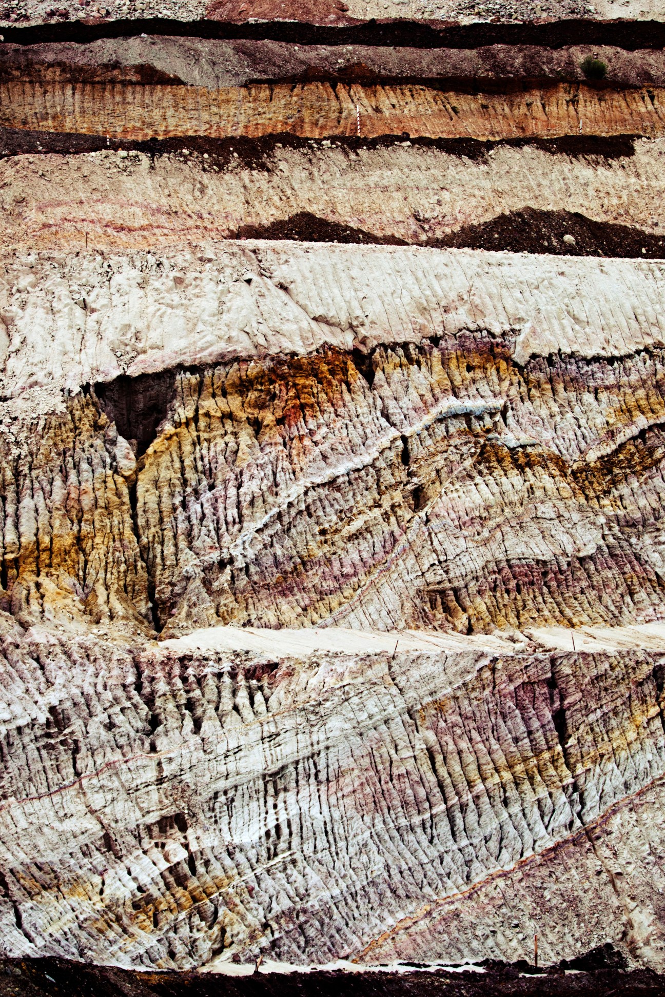 Layered rock strata in the walls of Greensnake Pit showing bands of whites, browns, reds and black manganese ore.