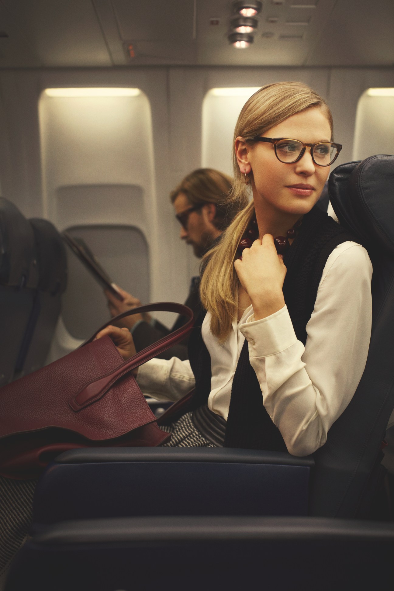 Woman in airplane cabin wearing Chanel glasses, Closed shirt, Zanone waistcoat, Hermès skirt and Tod's bag.