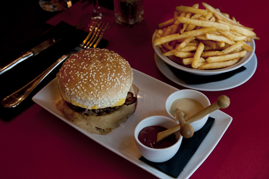 Ferdi restaurant burger meal with sesame seed bun, fries, and sauce on burgundy background.