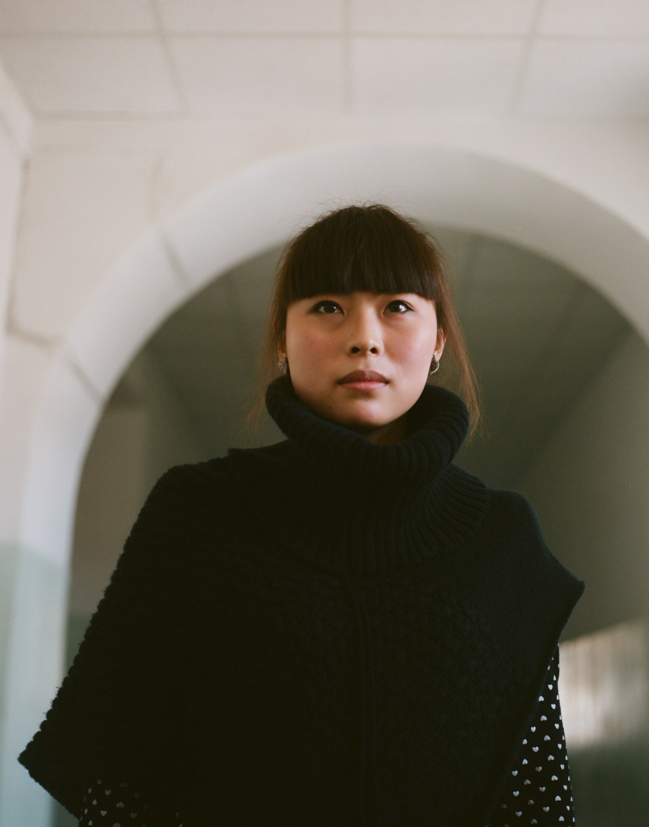 Wang Qi, 22, a Chinese student studying Russian in Blagoveshchensk, poses in an arched doorway wearing a black turtleneck.