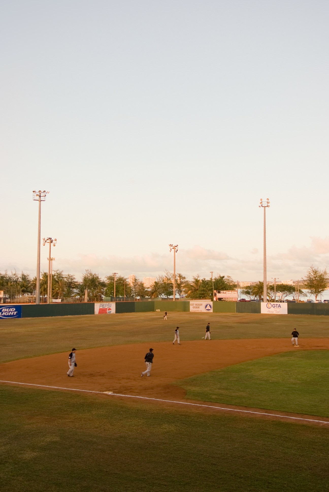 Baseball players on field at Paseo Baseball Stadium in Hagatña, Guam during sunset.