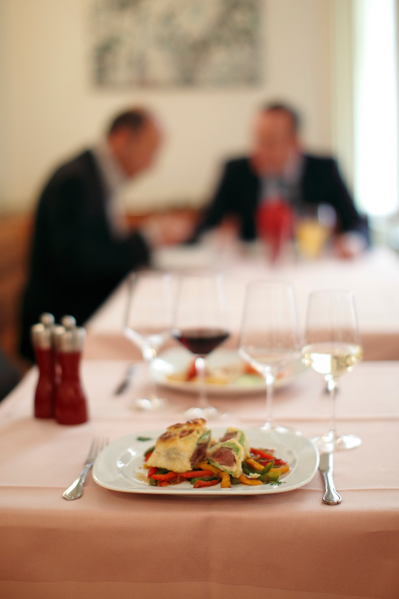 Fine dining table setting at Hebenstreit restaurant with plated dish, wine glasses, and diners in background.