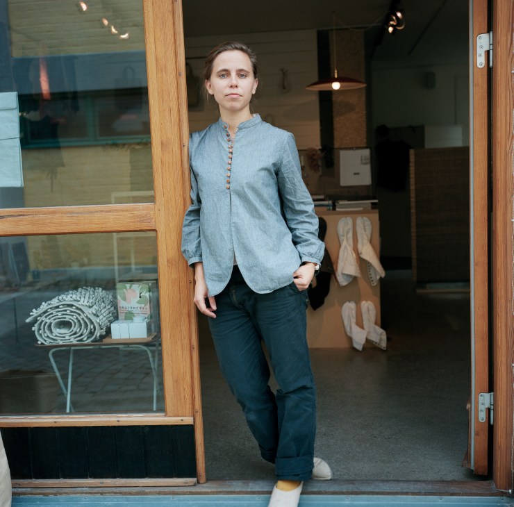 Woman standing in doorway of store displaying rolled textiles and woven goods in window display