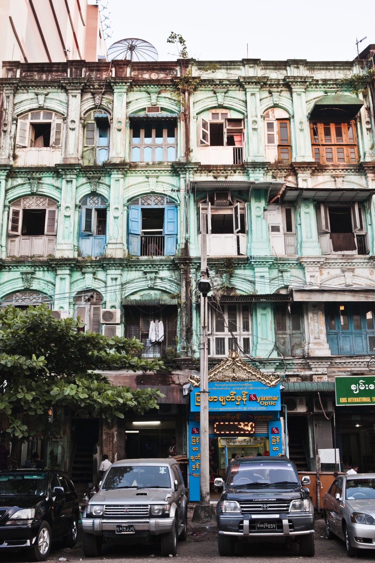 Deteriorating colonial building with mint-green and blue painted facade and arched windows in Rangoon's Little India neighbourhood.