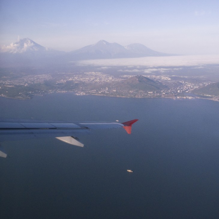 Aerial view of Petropavlovsk and Avacha Bay with Koryaksky volcano in background, seen from aircraft wing.