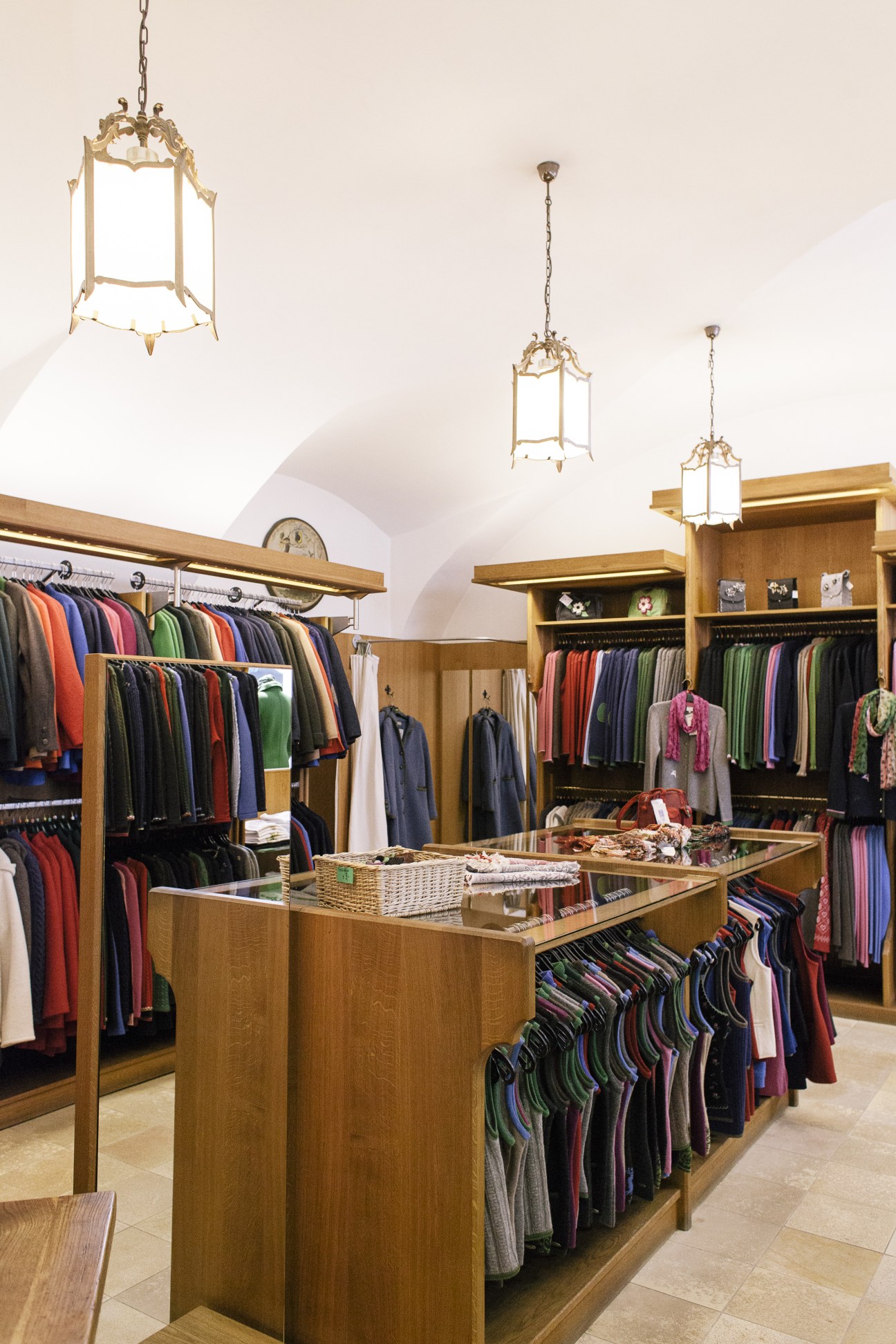 Interior of Loden Plankl traditional Austrian clothing store with wooden furnishings, hanging garments, and ornate pendant lighting.
