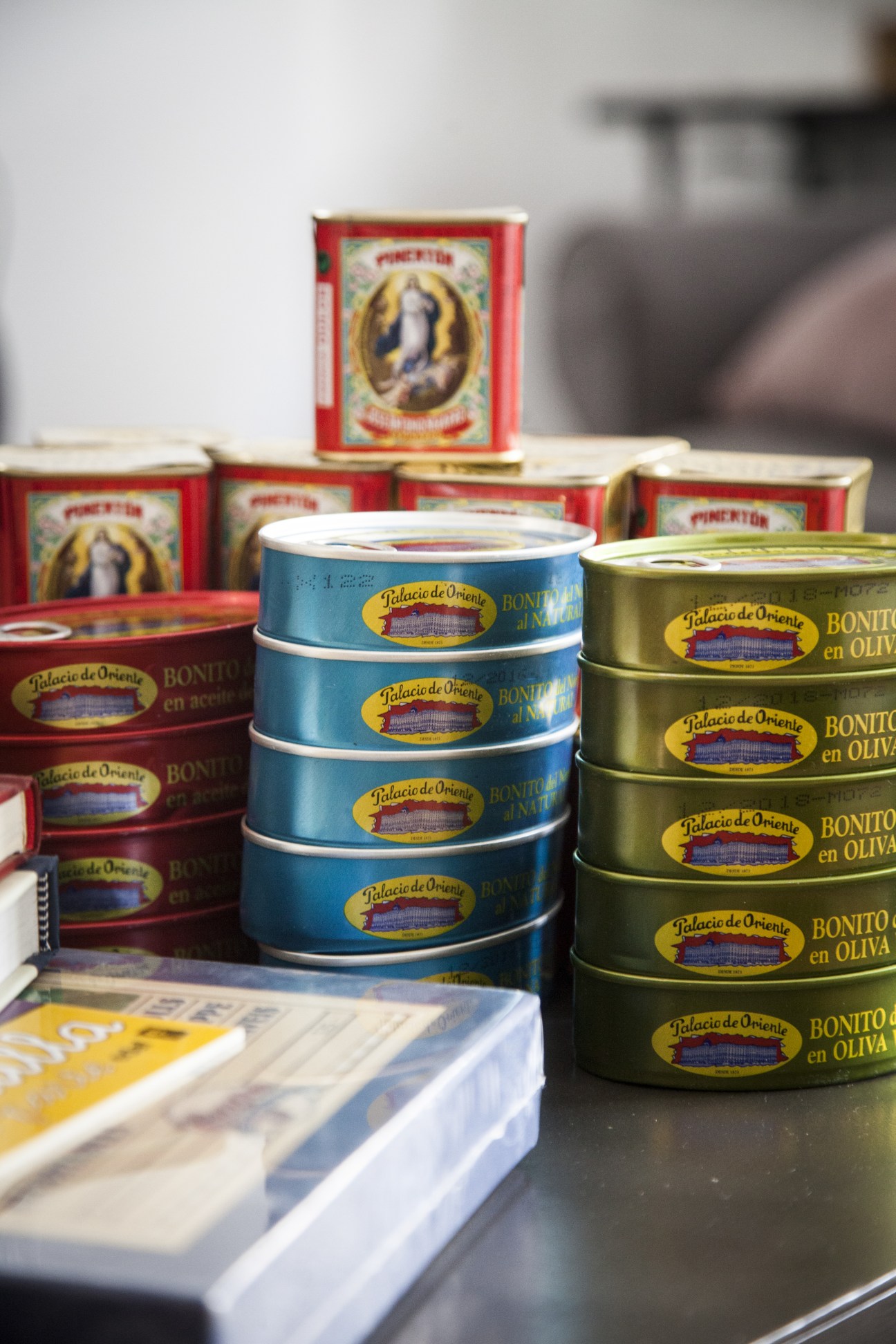 Stacked tins of Palacio de Oriente bonito and conserved food products in red, blue and olive-green packaging.
