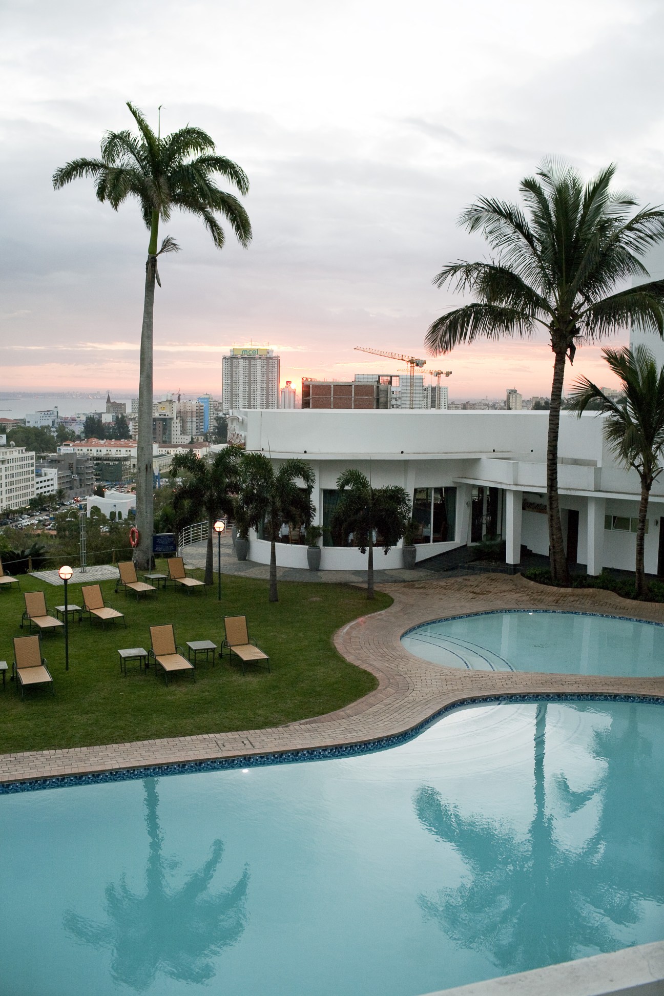 Hotel Cardoso pool and terrace overlooking Maputo cityscape at sunset with palm trees and construction cranes.