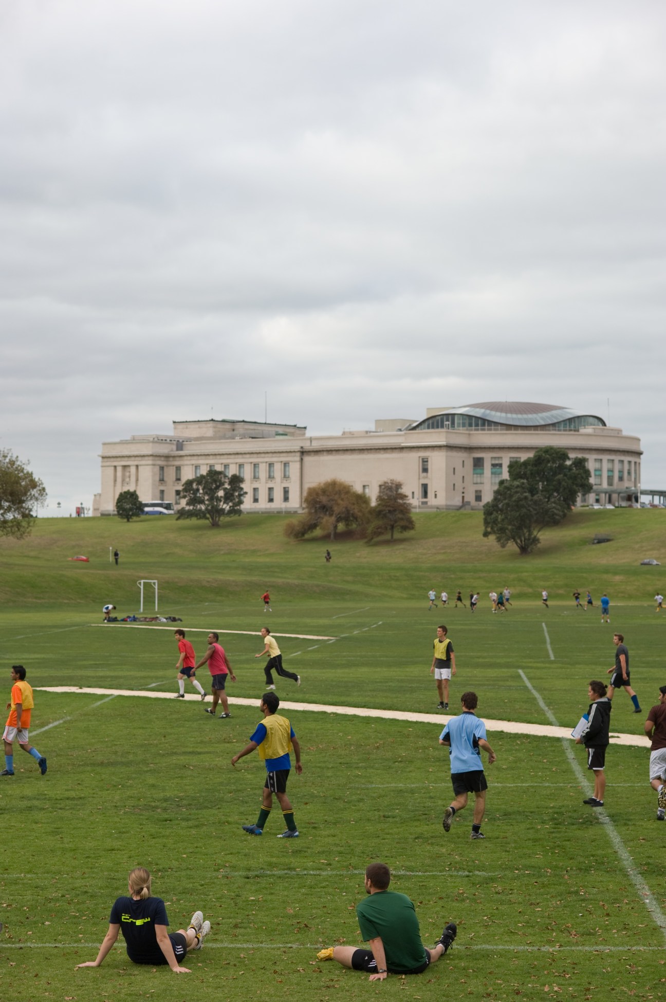 Children playing football on a grass field with Auckland Museum visible in the background.