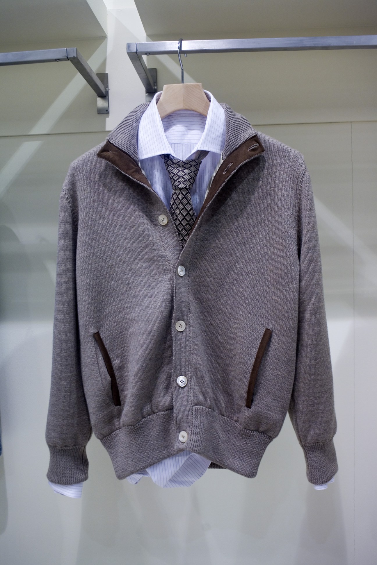 Pratoni cardigan in grey layered with striped shirt and patterned tie on wooden hanger.