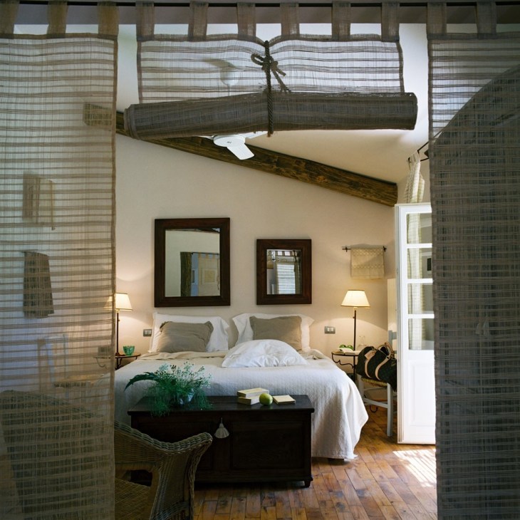 Bedroom interior at Poggio ai Santi with white bed, wooden beams, and neutral decor.