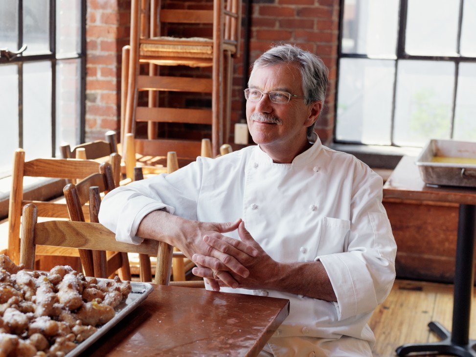 Chef Sam Hayward in white chef's coat at Fore Street restaurant with baked goods on table