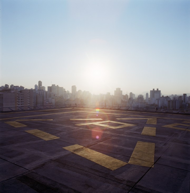 São Paulo skyline at sunset viewed from a rooftop helipad with yellow markings.