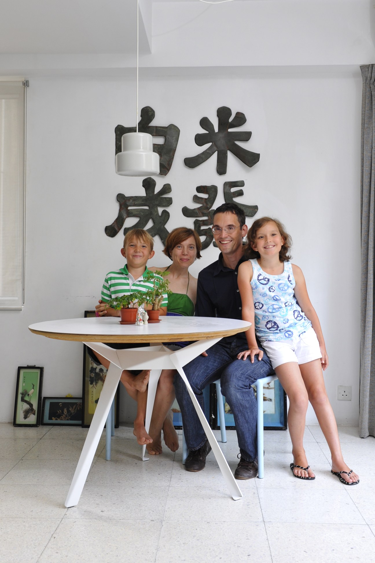 Esther van Wijck and Sjoerd Hoekstra with children Aard and Sim seated at a round white table in a bright apartment with Chinese calligraphy on the wall.