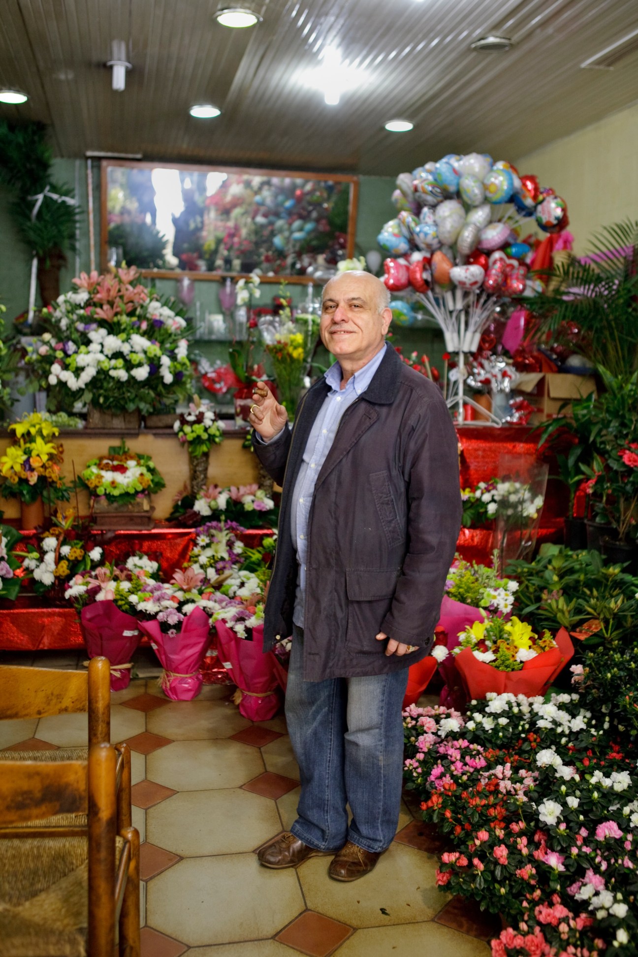 George Hanna, owner of Les Trois Fleurs flower shop, standing among colorful floral arrangements and potted flowers.