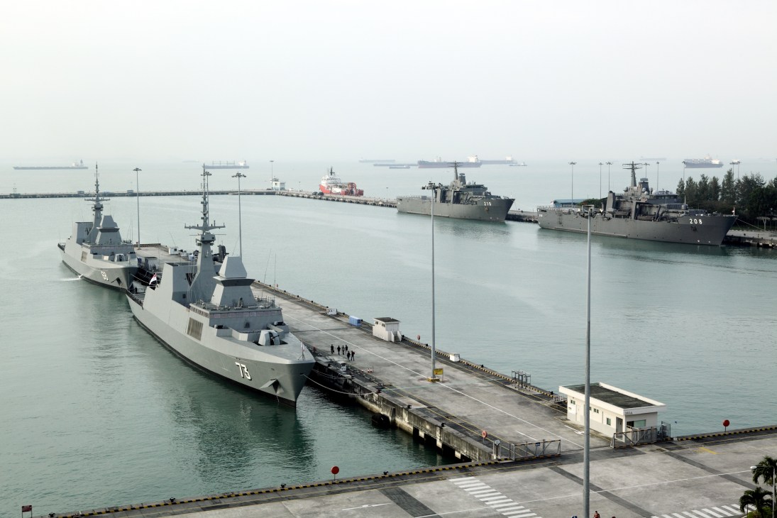 Multiple stealth frigates docked at Changi naval base with support vessels and cargo ships in the background.