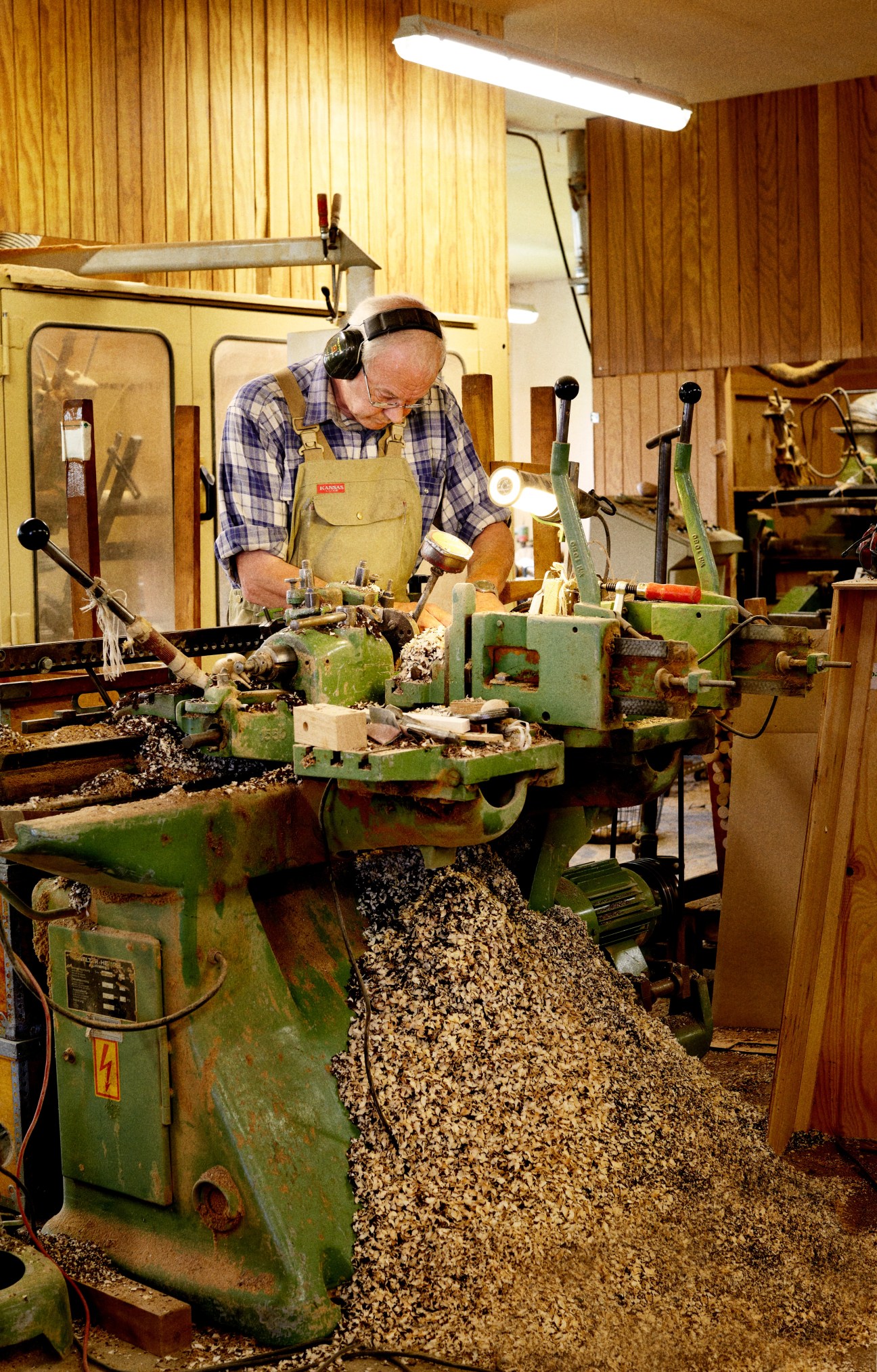 Craftsman Anker Villumsen operates a wood lathe in a workshop filled with wood shavings and traditional woodturning equipment.