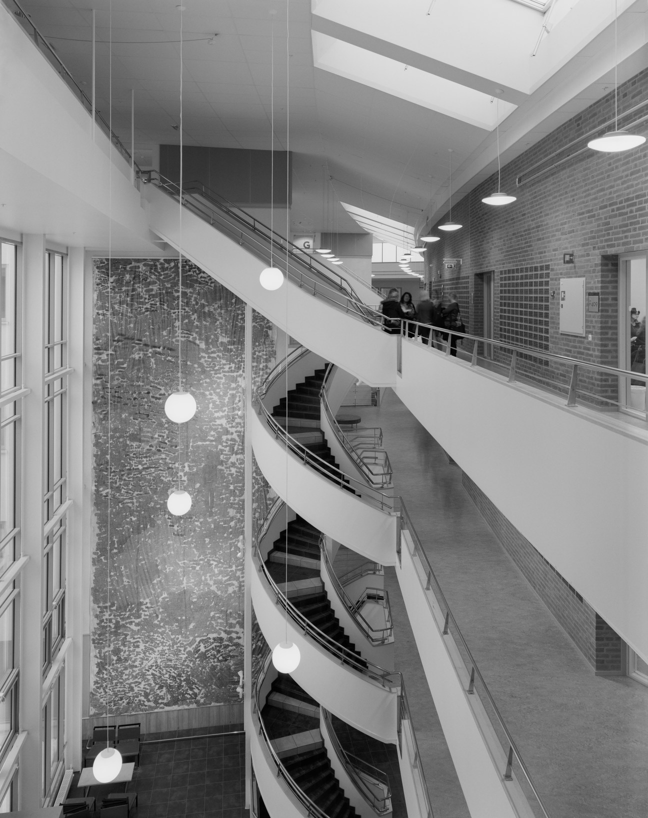 Interior view of Väst university showing modern spiral staircase with white railings, brick wall, and hanging pendant lights.