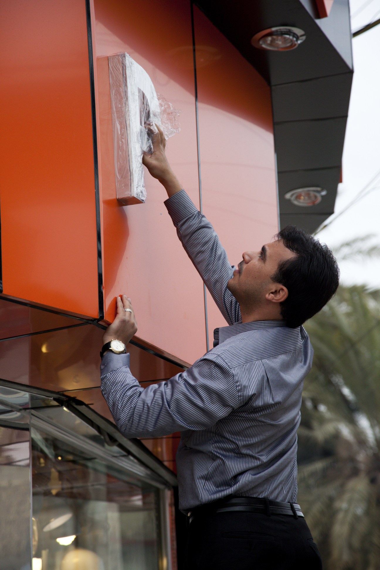 Man in blue striped shirt applying white plaster or compound to an orange-red wall panel.