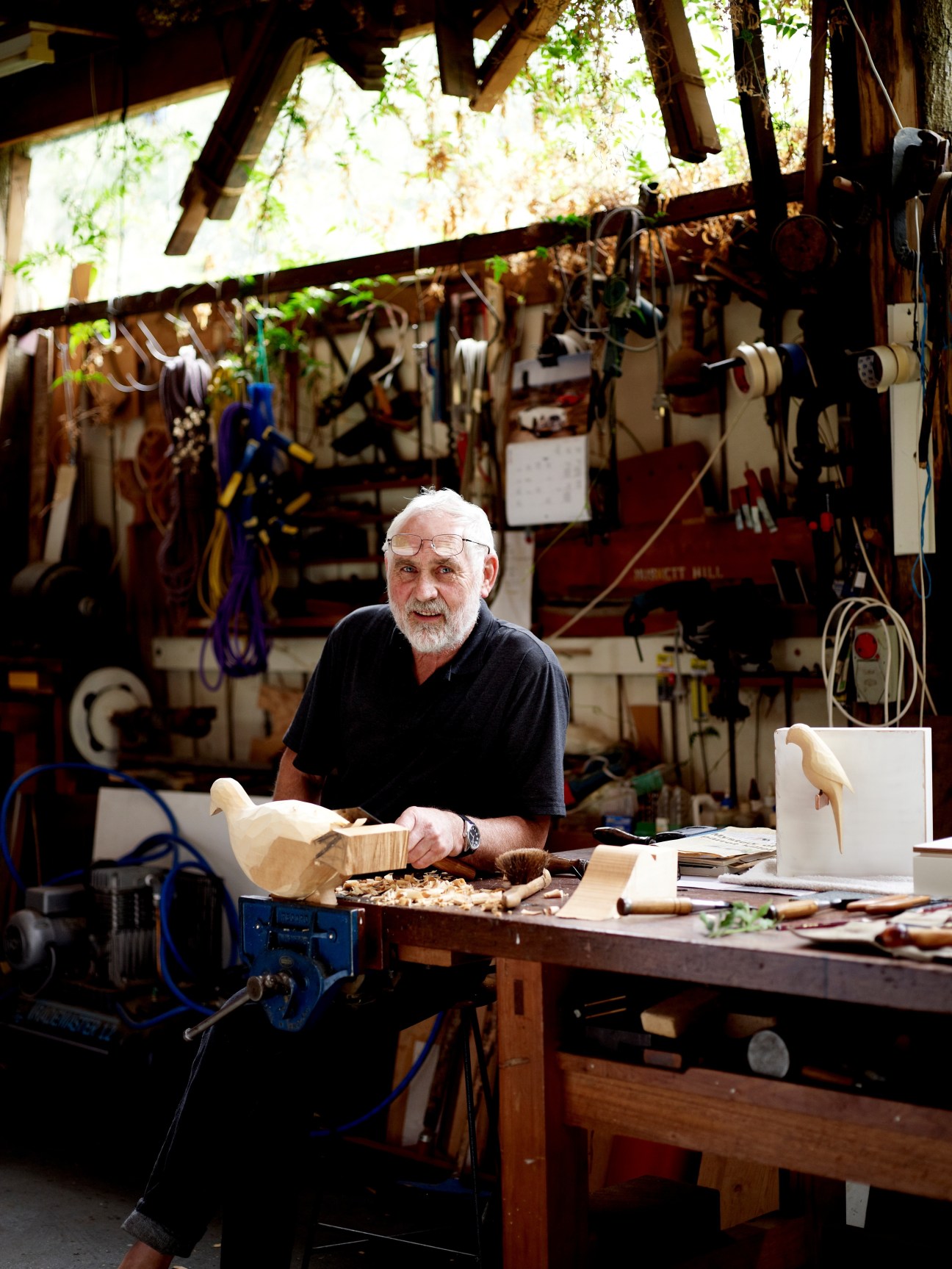 Kevin Perkins carving wooden birds in his workshop surrounded by tools and materials.