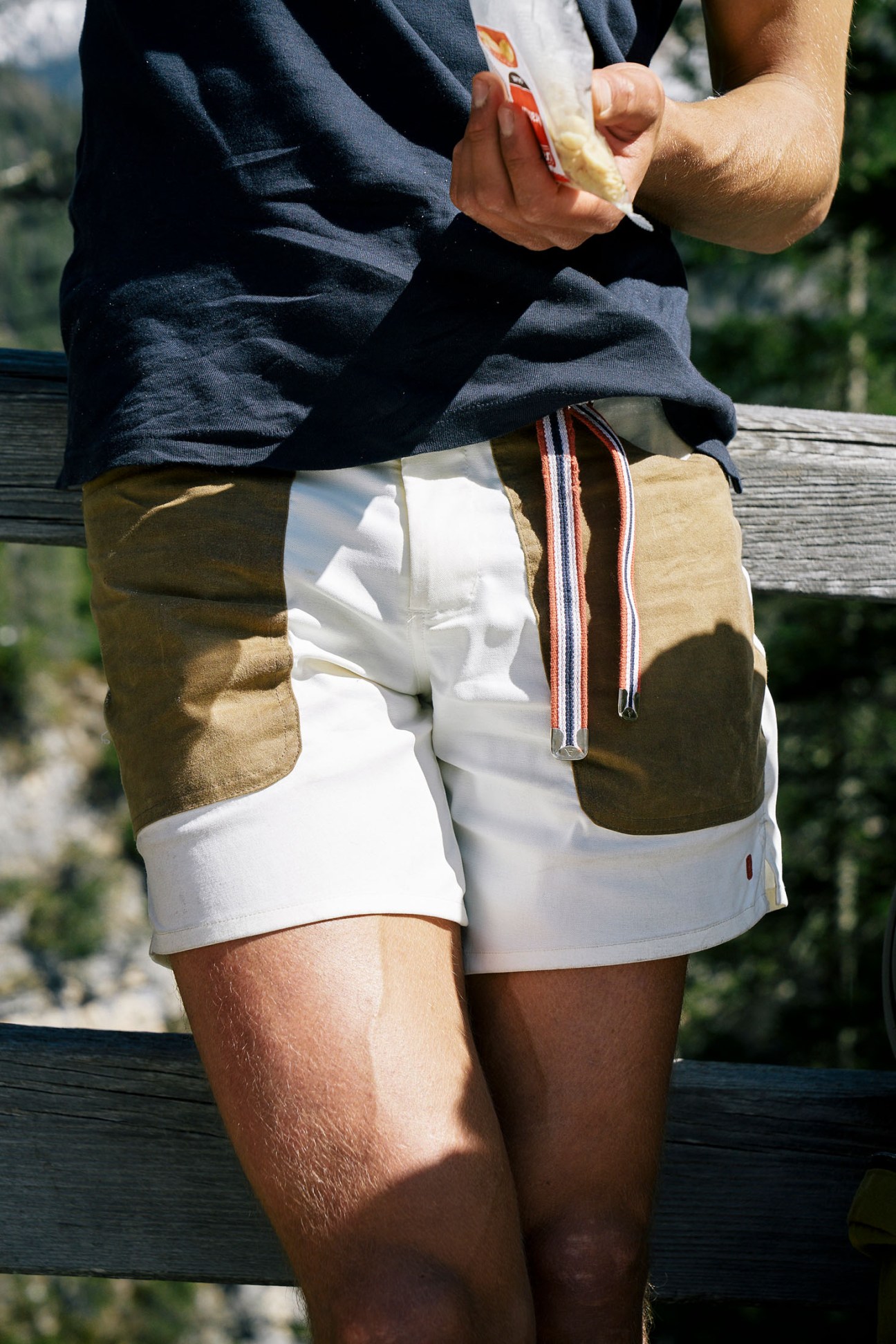 Person in white and khaki shorts holding a snack while sitting outdoors