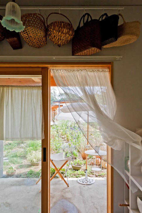 View through open glass doors to a resident's patio with chair, potted plants, and garden beyond at Yuimarl Nasu.