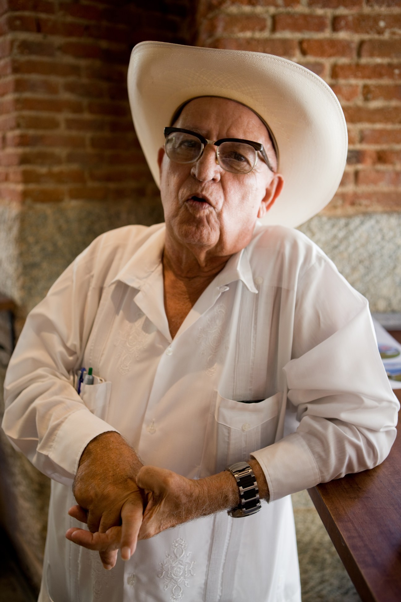 Orlando Laguardiá, a 69-year-old Cuban poet, wearing a white cowboy hat and white shirt against a brick wall.