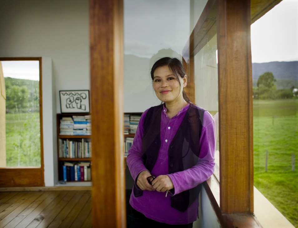 Artist Christina Chow stands in a modern home corridor with wooden frames and countryside views.