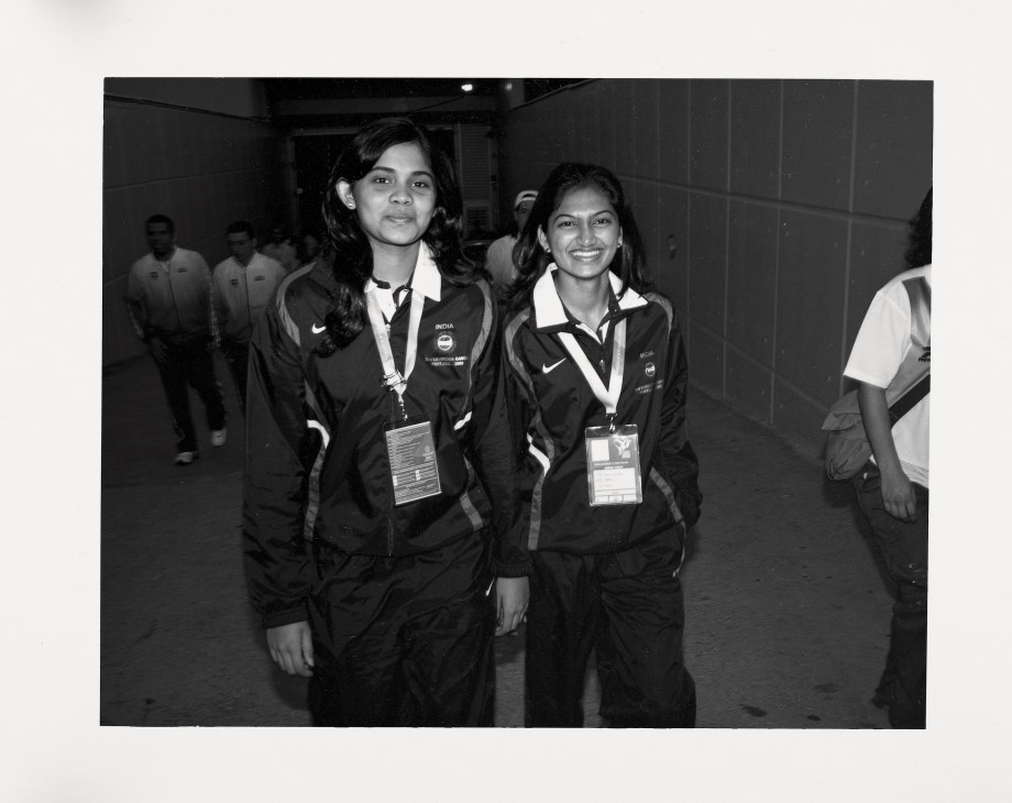Indian track team members in black Nike uniforms with credentials walking together.