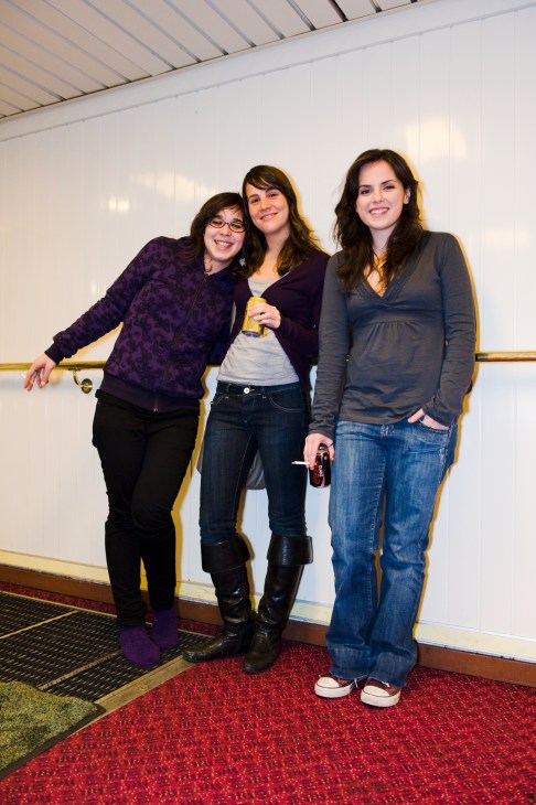 Three women posing together in a ship corridor, holding drinks.