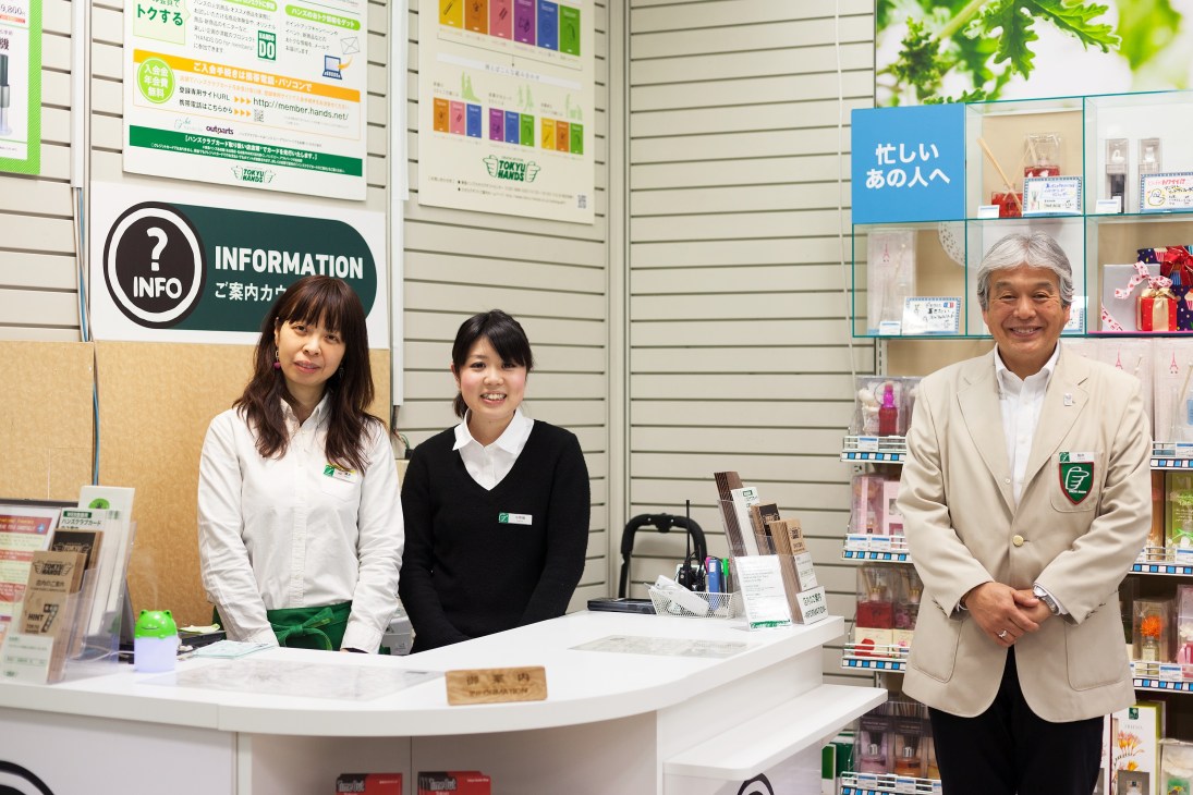 Three Tokyu Hands staff members at the information desk wearing green and white uniforms.