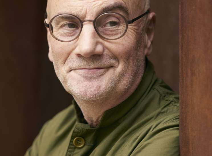 Portrait of Adrian Shaughnessy, a bald man with glasses wearing a green jacket.
