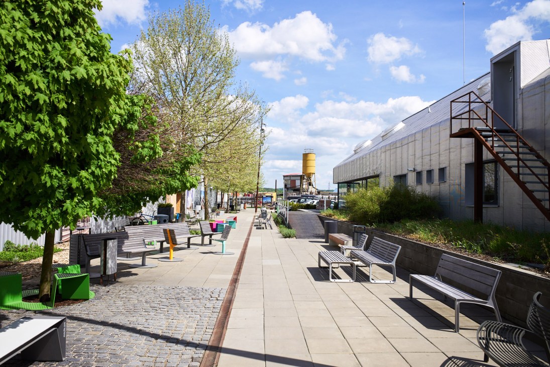 Mmcité's open-air showroom pathway lined with benches, bike racks and trees between converted farm buildings.