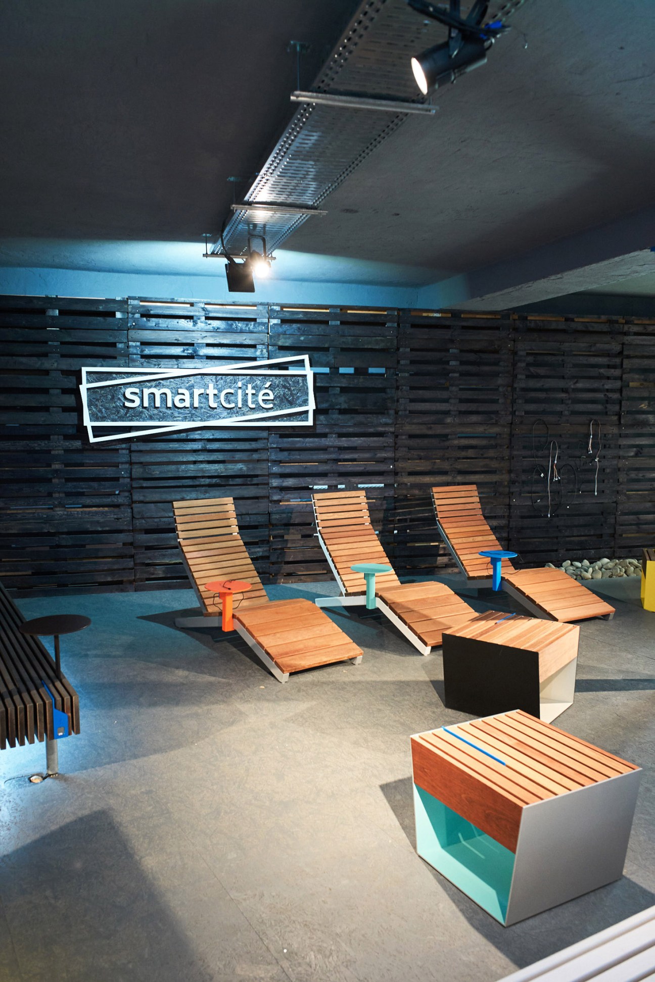 Mmcité's Smartcite street furniture with orange wooden seating, charging points, and LED backlights in a showroom setting.