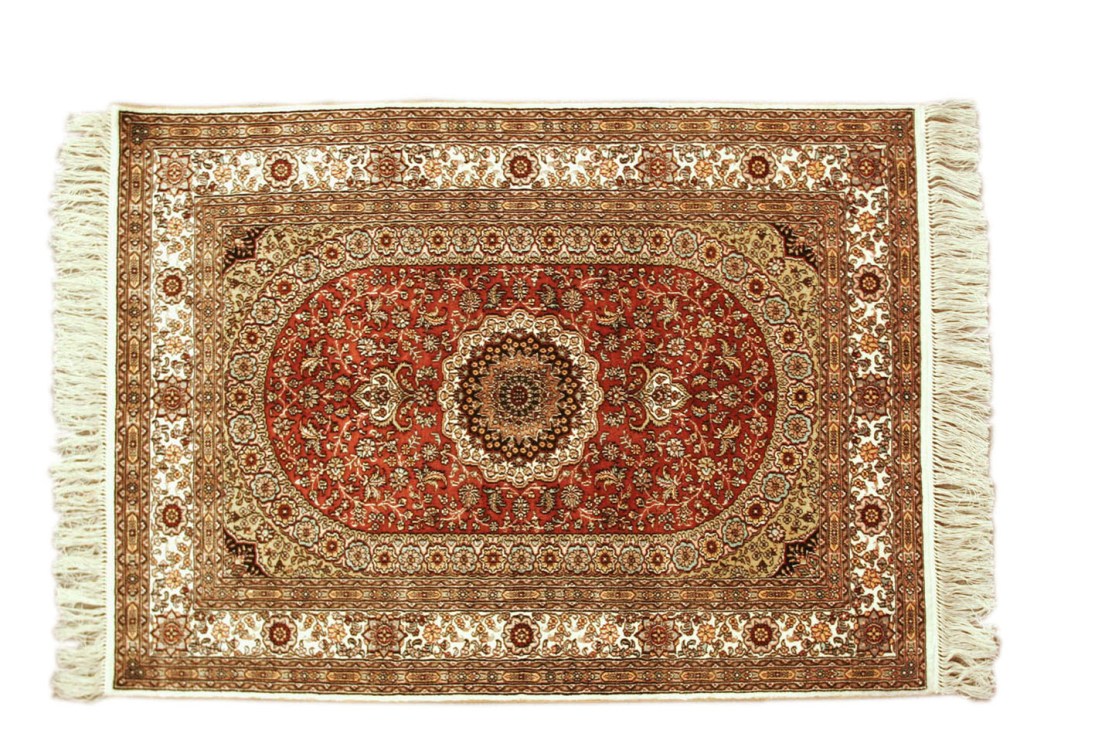Persian silk rug with red field, ornate central medallion and geometric border patterns with fringe edges.