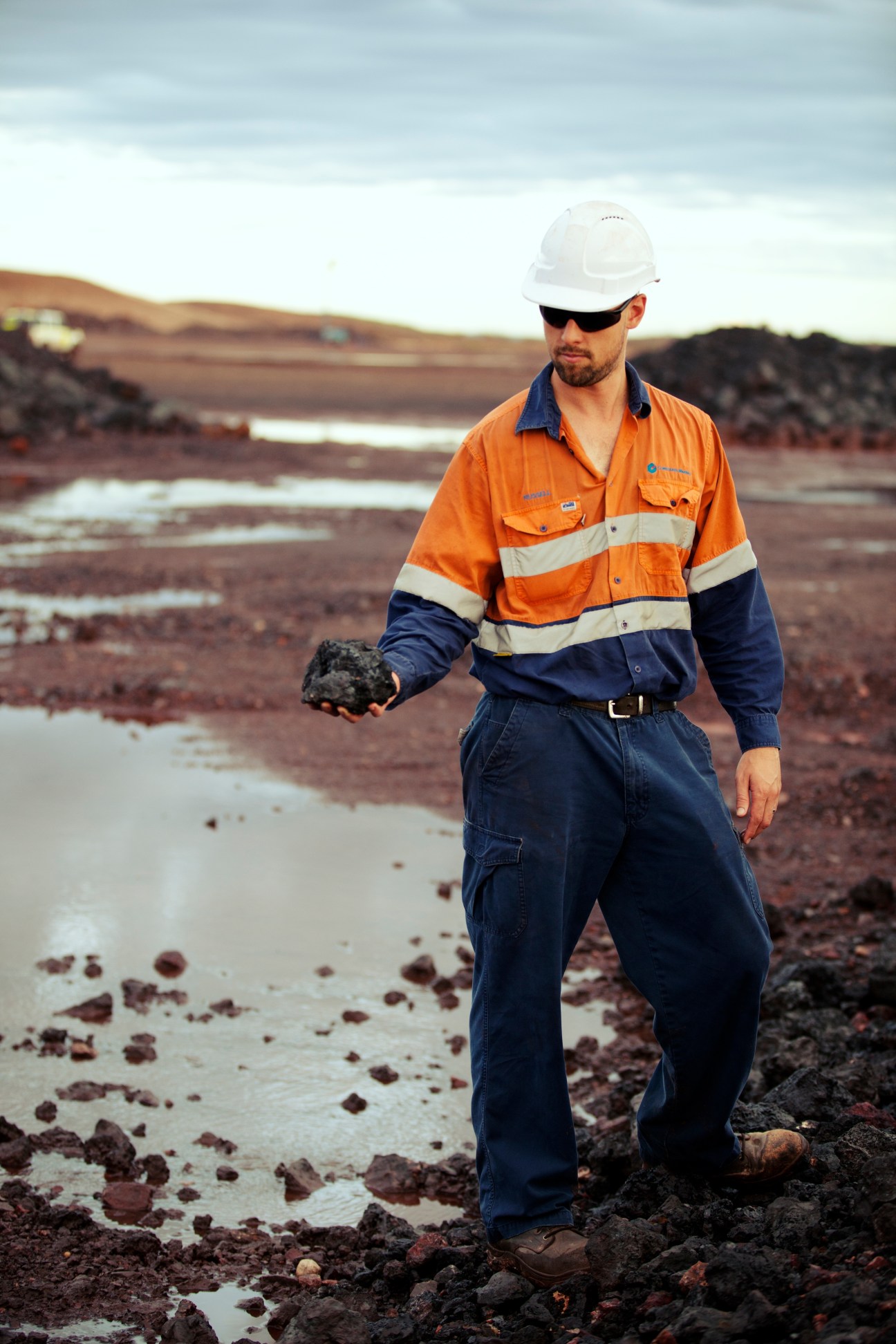 Mining worker in safety gear holds black manganese ore at an open pit mine site.