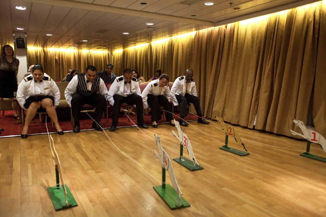 Ship officers in uniform playing a dog-sled pulling game in the main lounge of the RMS St Helena.