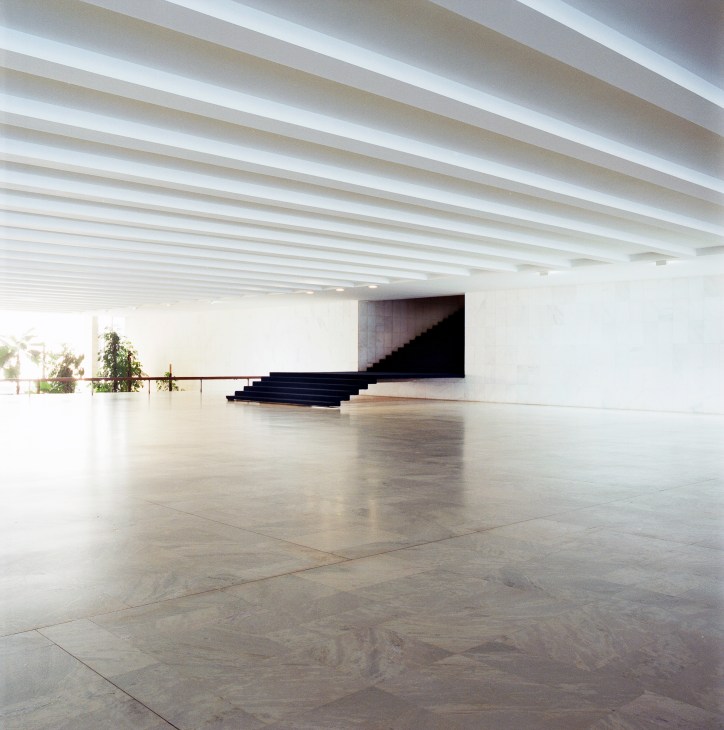 Modernist interior hallway with white ceiling, polished floor and dark staircase leading to upper level.