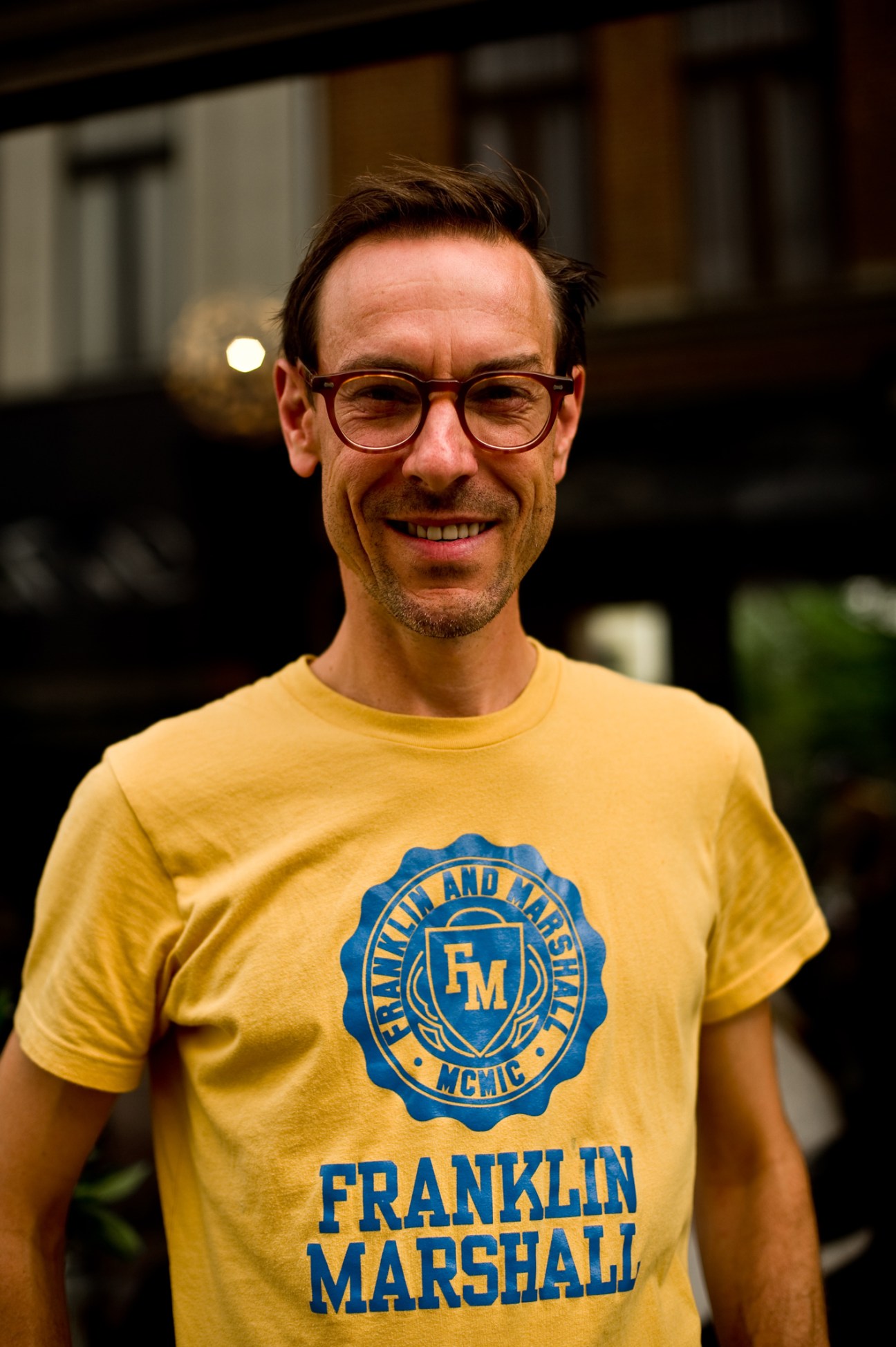 Rob Berghmans, owner of Caffènation, smiling at the camera wearing glasses and a yellow Franklin Marshall t-shirt.