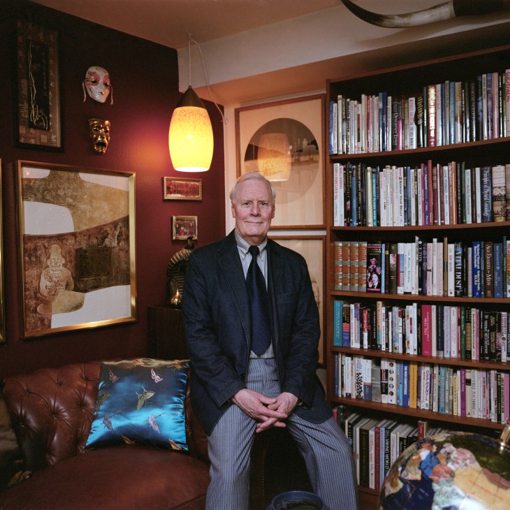 Jerry Nelson sits on a burgundy leather sofa in his Marina City studio apartment, surrounded by books, artwork, and collected objects.