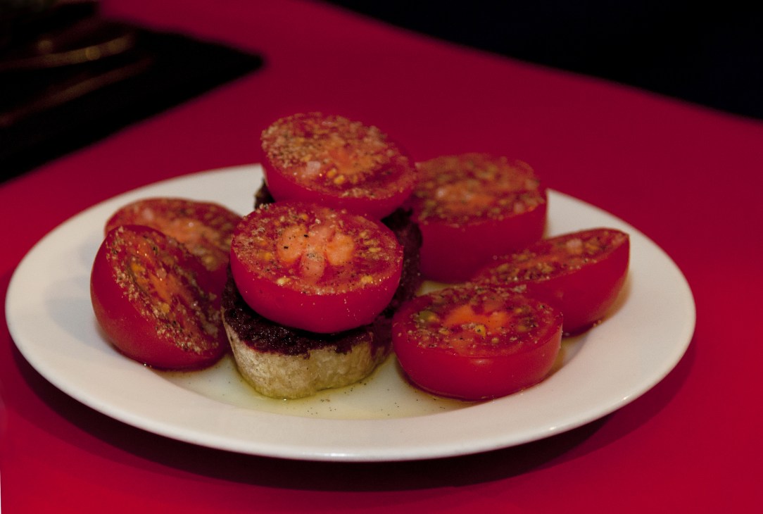 Plate of stuffed tomatoes with golden breadcrumb topping on white dish against magenta background.